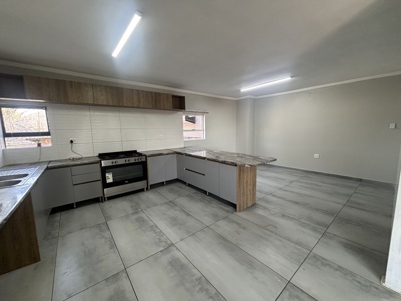 Modern open-plan kitchen featuring grey cabinetry, marble-look countertops, a freestanding stove, and large format floor tiles in a clean, vacant space.