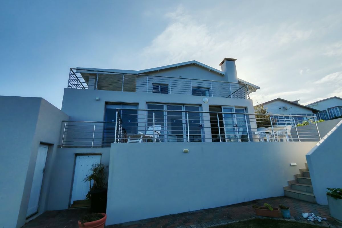 Rear elevation of a multi-level house featuring a spacious balcony with stainless steel railings, large sliding glass doors, and a paved patio area.