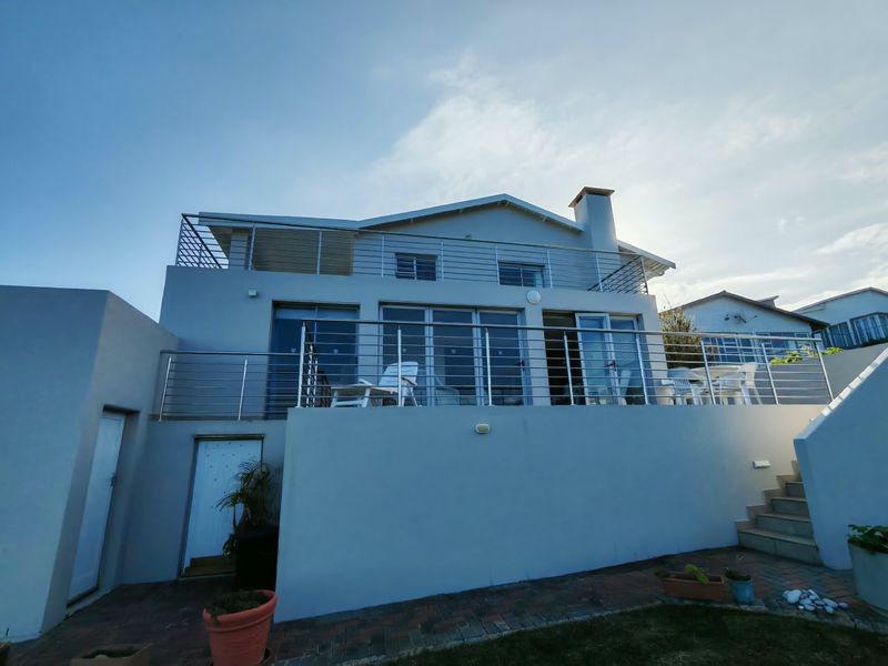 Rear elevation of a multi-level house featuring a spacious balcony with stainless steel railings, large sliding glass doors, and a paved patio area.