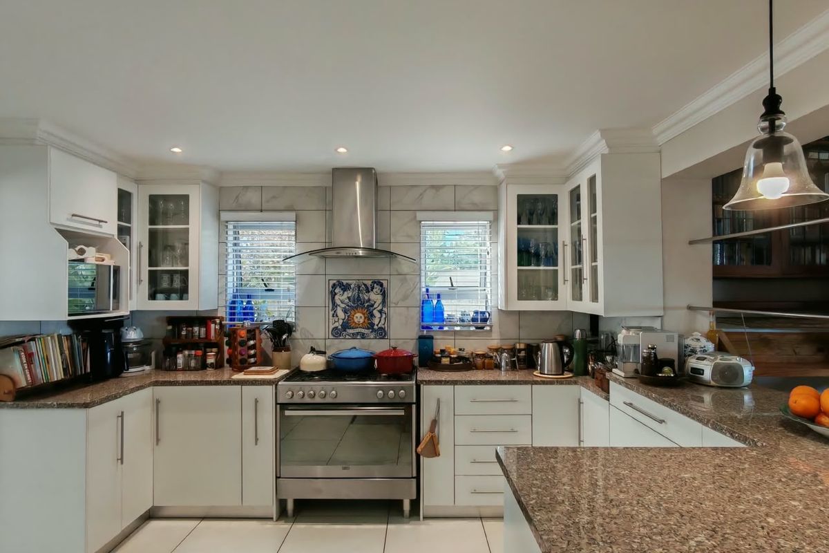 A well-maintained kitchen featuring granite countertops, white cabinetry, a stainless steel gas stove with extractor fan, and tiled flooring.