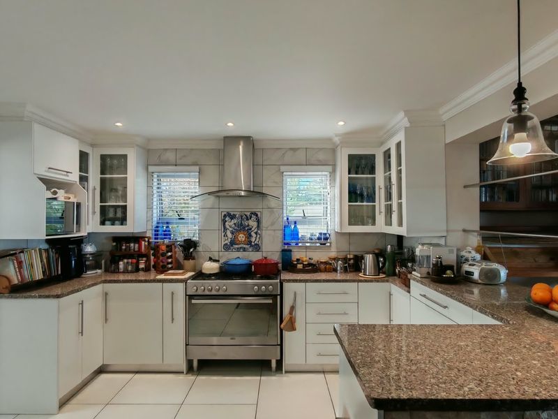A well-maintained kitchen featuring granite countertops, white cabinetry, a stainless steel gas stove with extractor fan, and tiled flooring.
