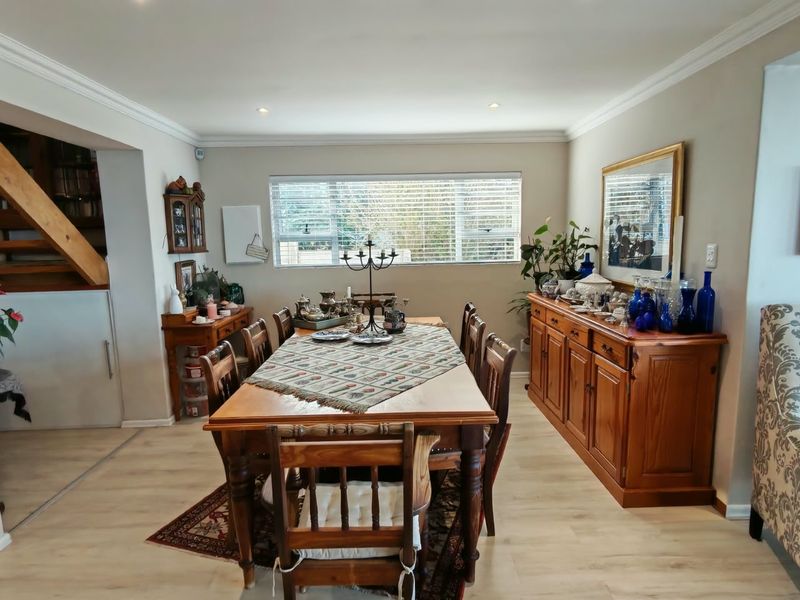 A well-maintained dining room featuring light laminate flooring, crown molding, recessed lighting, and a timber staircase leading to the upper level.