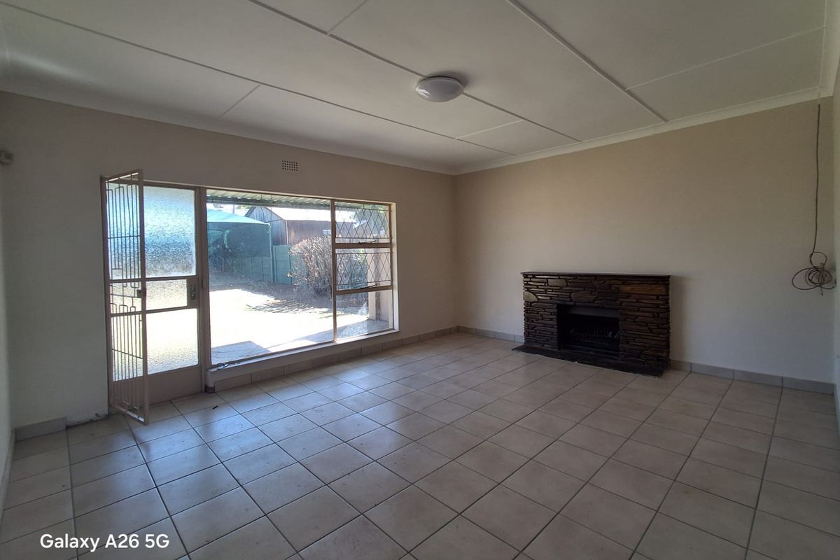 Spacious living room featuring tiled flooring, a stone-clad fireplace, and large windows providing natural light and access to the exterior.