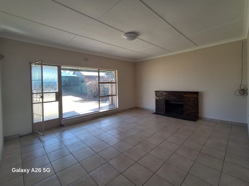 Spacious living room featuring tiled flooring, a stone-clad fireplace, and large windows providing natural light and access to the exterior.