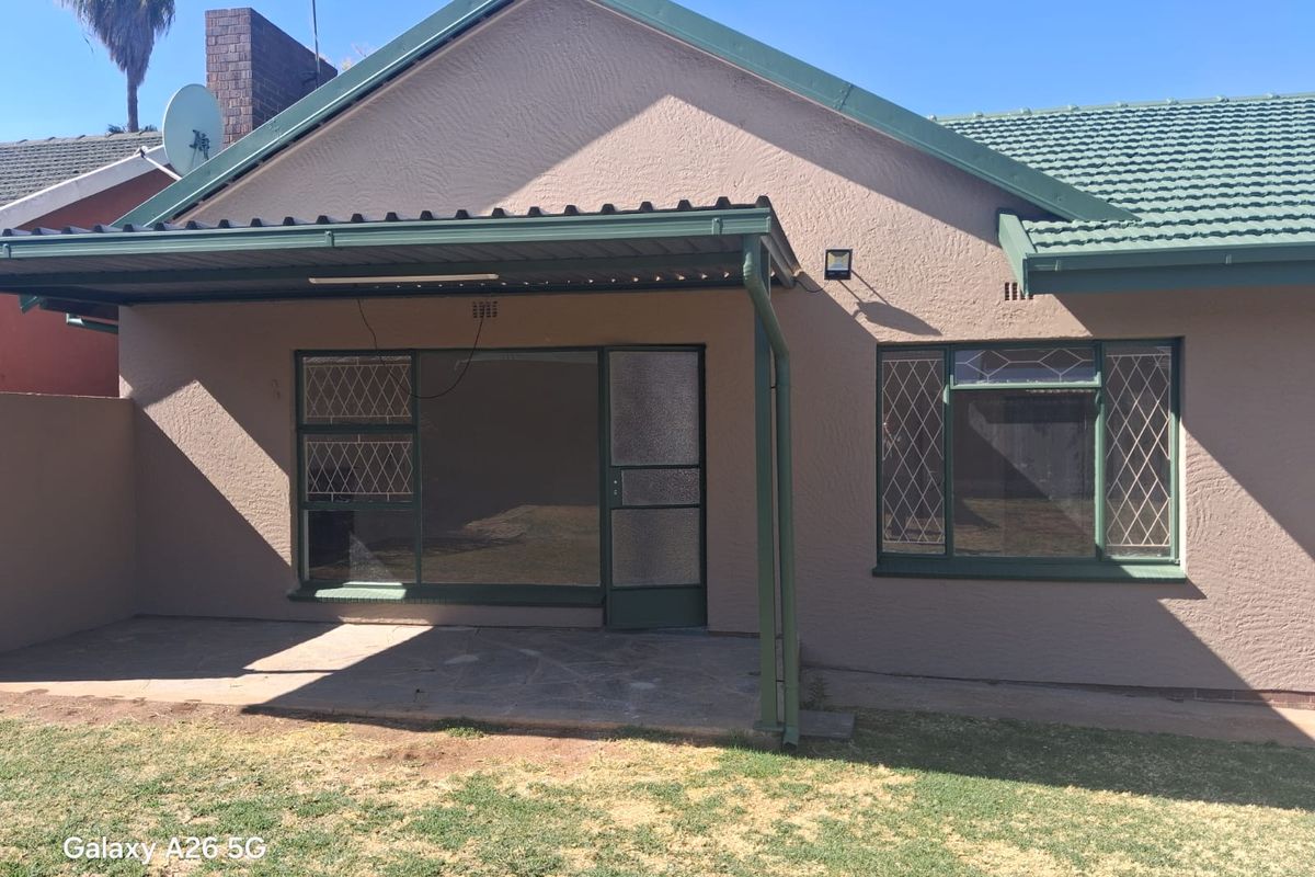 Rear view of the house featuring a covered patio area, tiled roof, and diamond pattern window security bars.