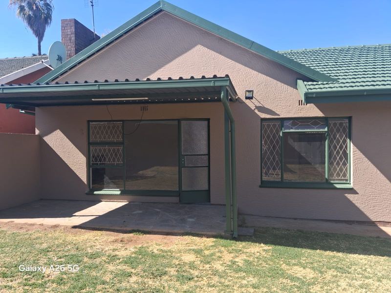 Rear view of the house featuring a covered patio area, tiled roof, and diamond pattern window security bars.