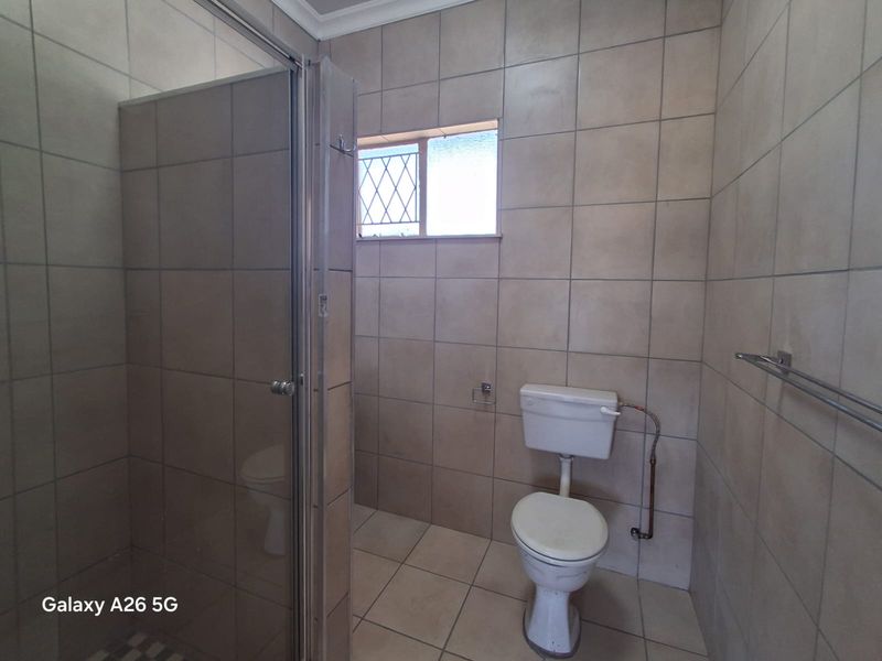 A functional bathroom featuring a shower enclosure, toilet, and neutral floor-to-ceiling tiling.
