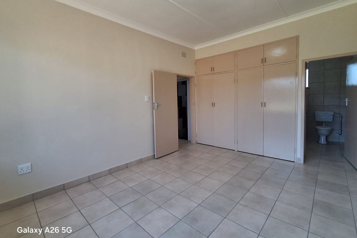 A spacious, empty bedroom featuring neutral tiled flooring, built-in cupboards, and direct access to an en-suite bathroom.