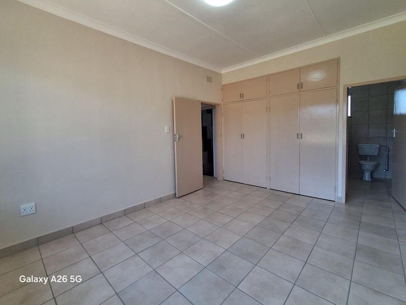 A spacious, empty bedroom featuring neutral tiled flooring, built-in cupboards, and direct access to an en-suite bathroom.