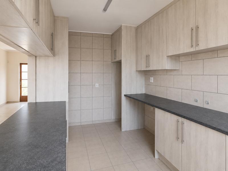 A clean, modern kitchen featuring light wood-tone cabinetry, dark countertops, and neutral ceramic tiling throughout, offering a functional and well-maintained workspace.