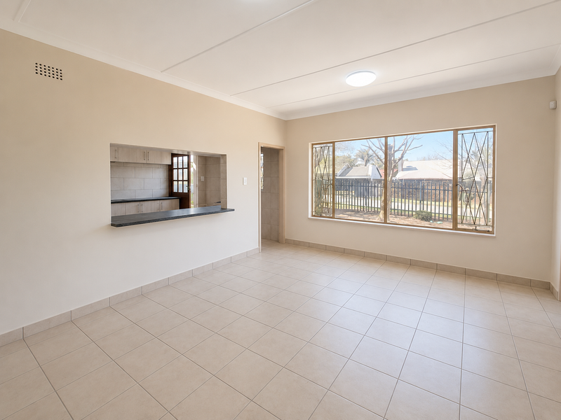 A bright and spacious living area featuring neutral tiled flooring, a convenient serving hatch to the kitchen, and large windows with security bars.