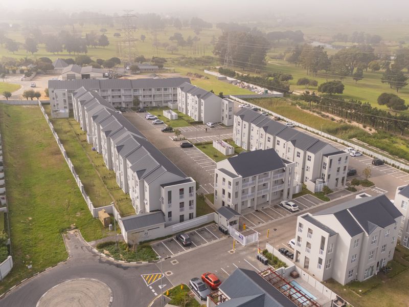 Aerial view of a modern apartment complex featuring multiple residential blocks, paved parking areas, and secure perimeter fencing.