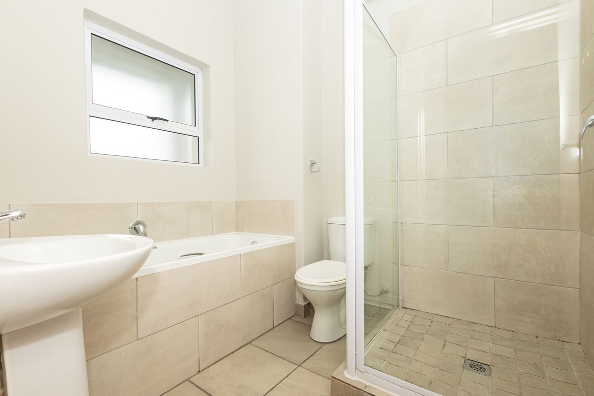 A clean, modern bathroom featuring a pedestal basin, a built-in bathtub, a separate glass-enclosed shower, and neutral floor-to-ceiling tiling.