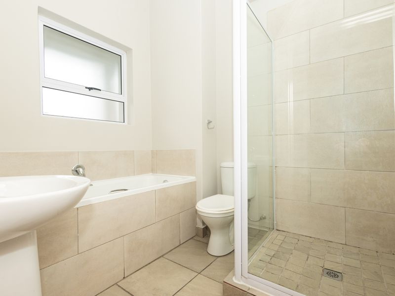 A clean, modern bathroom featuring a pedestal basin, a built-in bathtub, a separate glass-enclosed shower, and neutral floor-to-ceiling tiling.