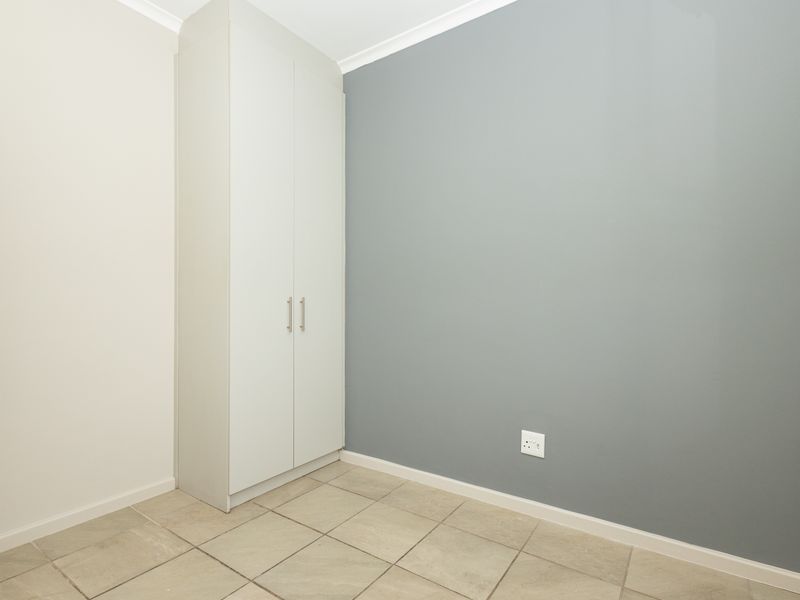 A clean, empty bedroom featuring neutral tiled flooring, a built-in wardrobe, and a modern grey accent wall.