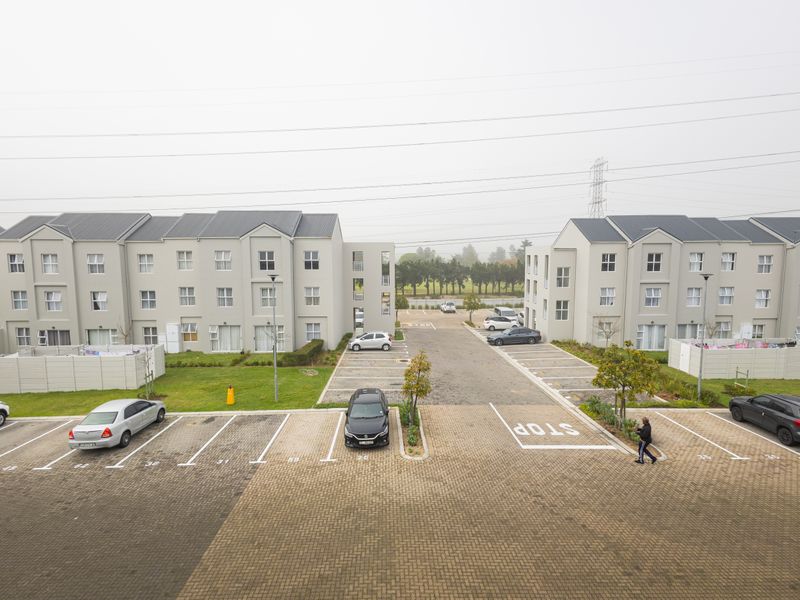 An aerial view of a modern apartment complex featuring paved parking bays, landscaped green spaces, and well-maintained multi-story residential buildings.