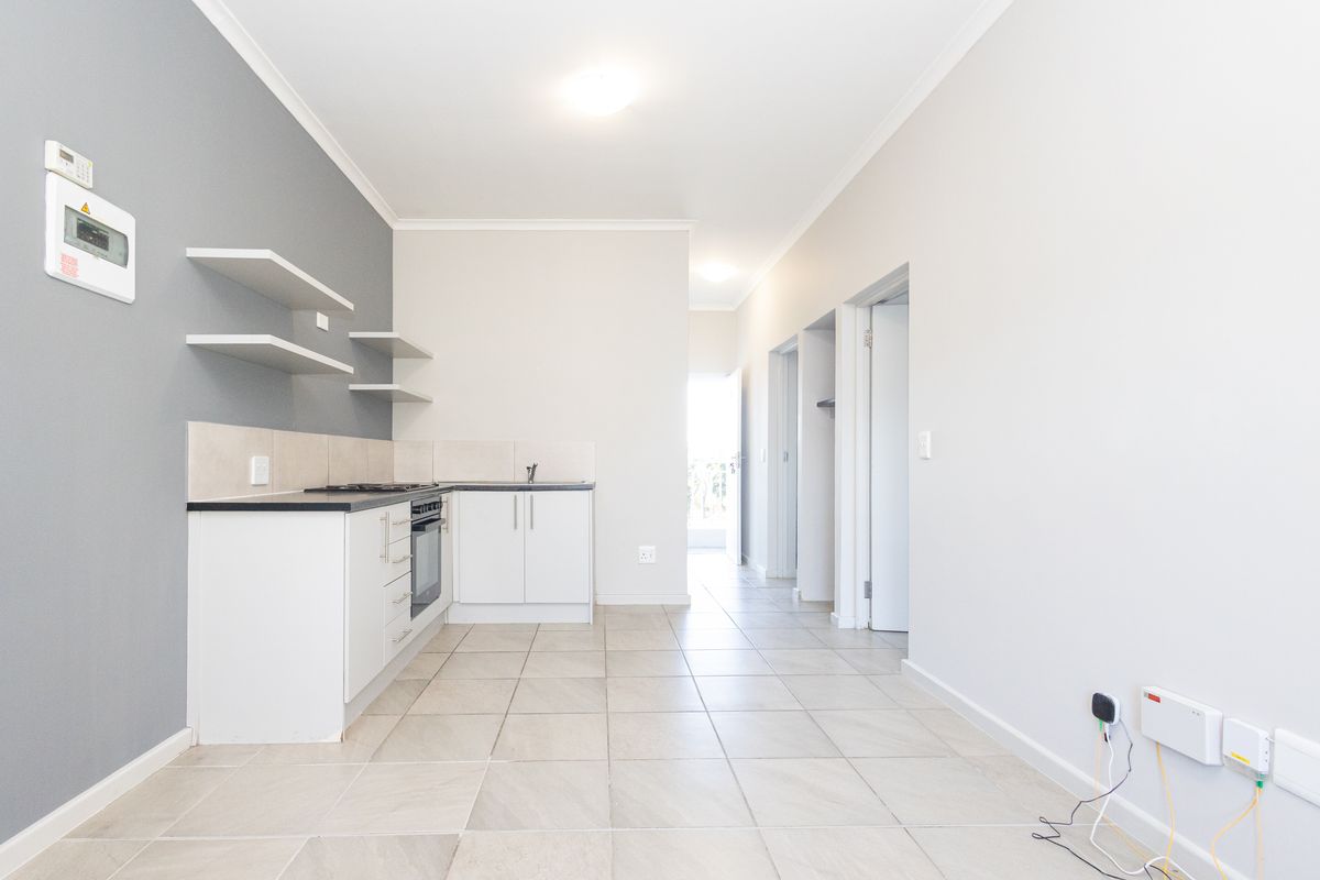 Open-plan kitchen area featuring modern white cabinetry, built-in oven, hob, and neutral tiled flooring, leading into a hallway.