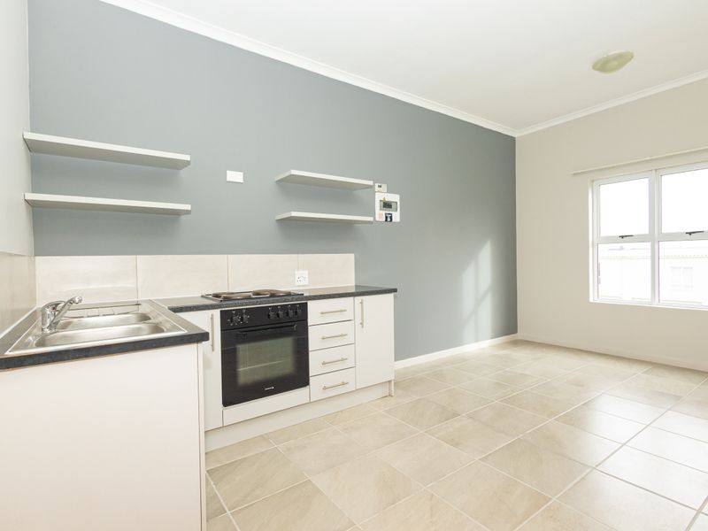 A clean, empty kitchen featuring tiled flooring, built-in oven and hob, stainless steel sink, and floating wall shelves.
