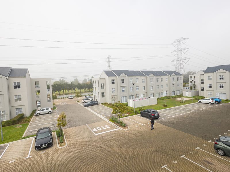 An elevated aerial view of a modern apartment complex featuring paved parking bays, landscaped garden areas, and multi-story residential buildings.