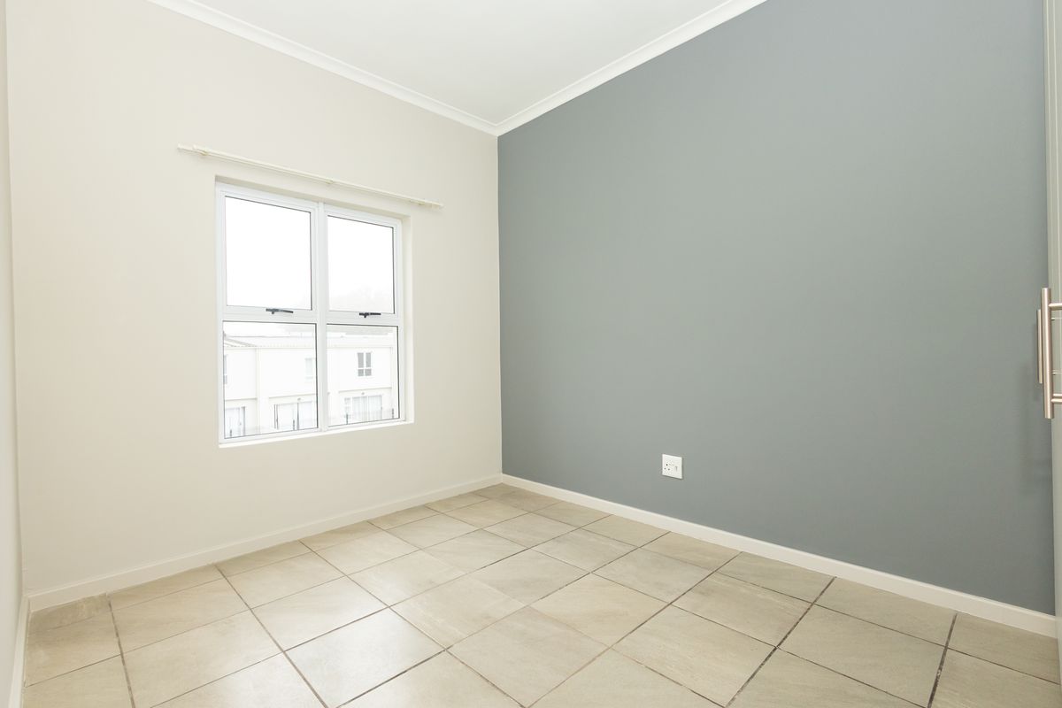 A bright, empty bedroom featuring neutral tiled flooring, a grey accent wall, and a built-in cupboard, offering a clean and versatile living space.