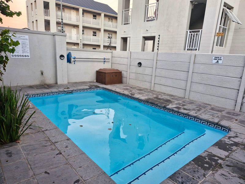 A private swimming pool area featuring stone paving and secure perimeter walling with electric fencing in an apartment complex setting.
