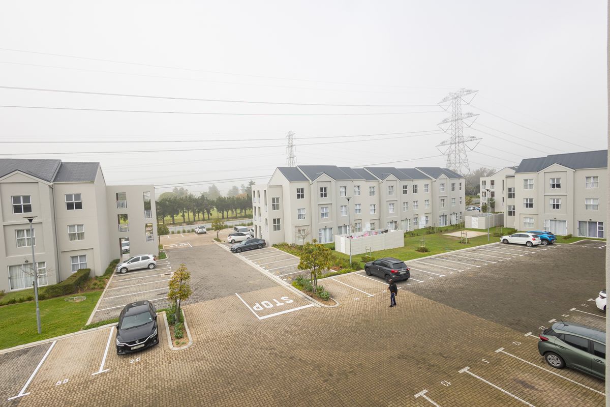 An elevated aerial view of a modern apartment complex featuring paved parking bays, landscaped garden areas, and multi-story residential buildings.