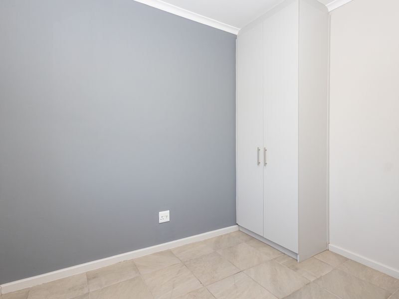 A clean, empty bedroom featuring neutral grey accent wall, built-in white wardrobe, and tiled flooring.