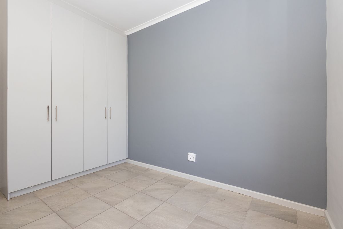 A clean, empty bedroom featuring neutral grey walls, tiled flooring, and ample built-in cupboard storage space.