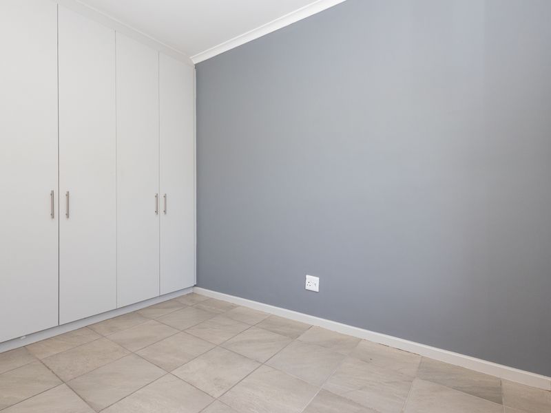 A clean, empty bedroom featuring neutral grey walls, tiled flooring, and ample built-in cupboard storage space.