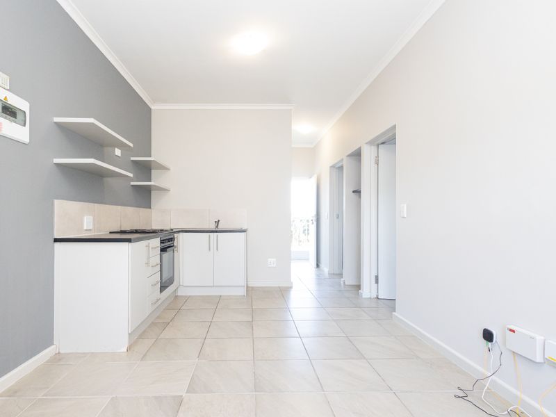 Open-plan kitchen area featuring modern white cabinetry, built-in oven, hob, and neutral tiled flooring, leading into a hallway.