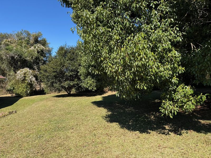 A spacious, well-maintained garden area featuring established mature trees and a grassy lawn, providing a private outdoor setting.
