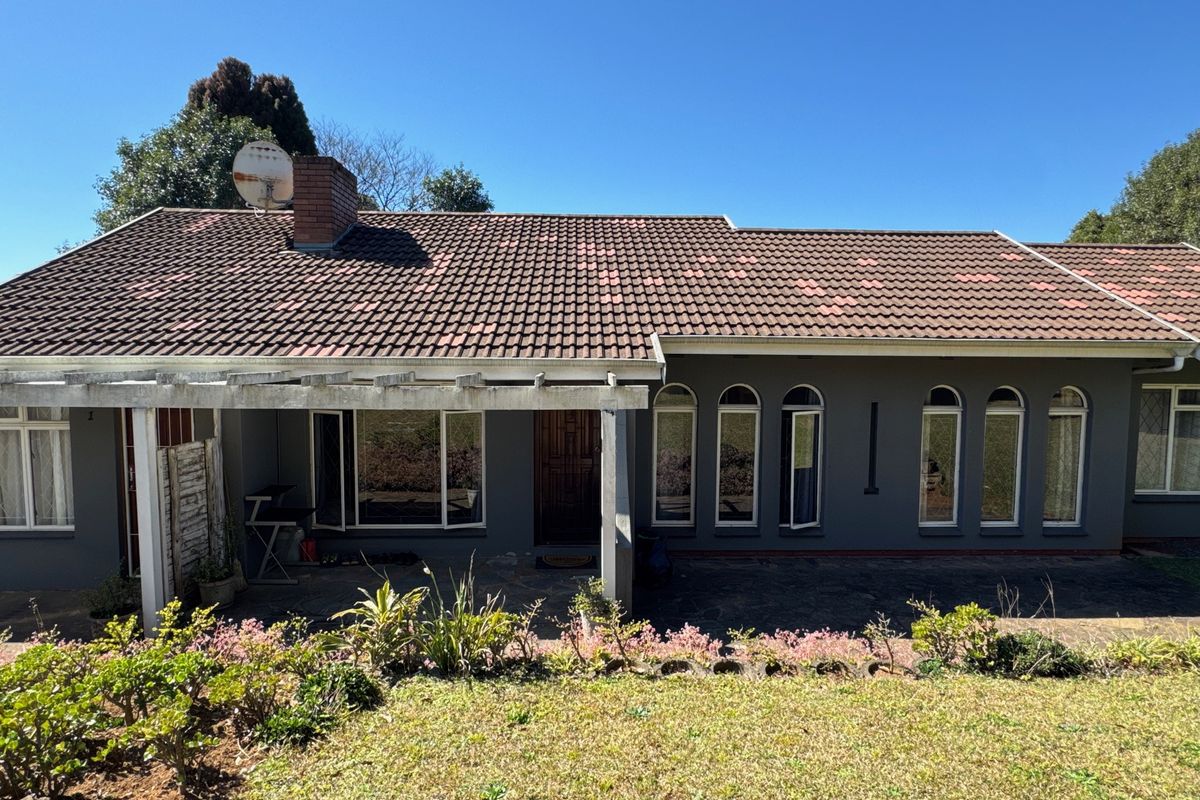 Rear view of the cottage featuring a covered patio with timber pergola, arched windows, and a tiled roof with a brick chimney.