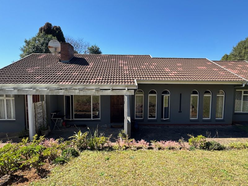 Rear view of the cottage featuring a covered patio with timber pergola, arched windows, and a tiled roof with a brick chimney.