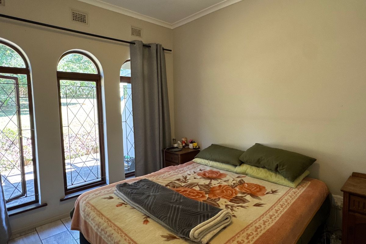 A bedroom featuring arched windows with leaded glass detailing, tiled flooring, and neutral wall finishes, providing direct access to the exterior.