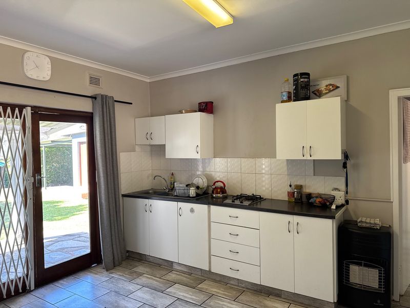 Compact kitchen featuring white cabinetry, dark countertops, gas hob, and tiled backsplash, with direct access to the outdoor patio area.