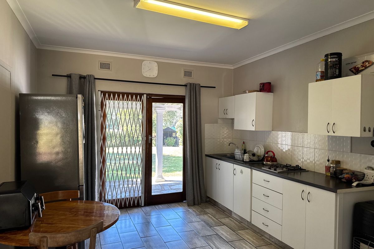 Functional kitchen featuring white cabinetry, gas hob, tiled splashback, and direct access to the rear garden through a sliding glass door.