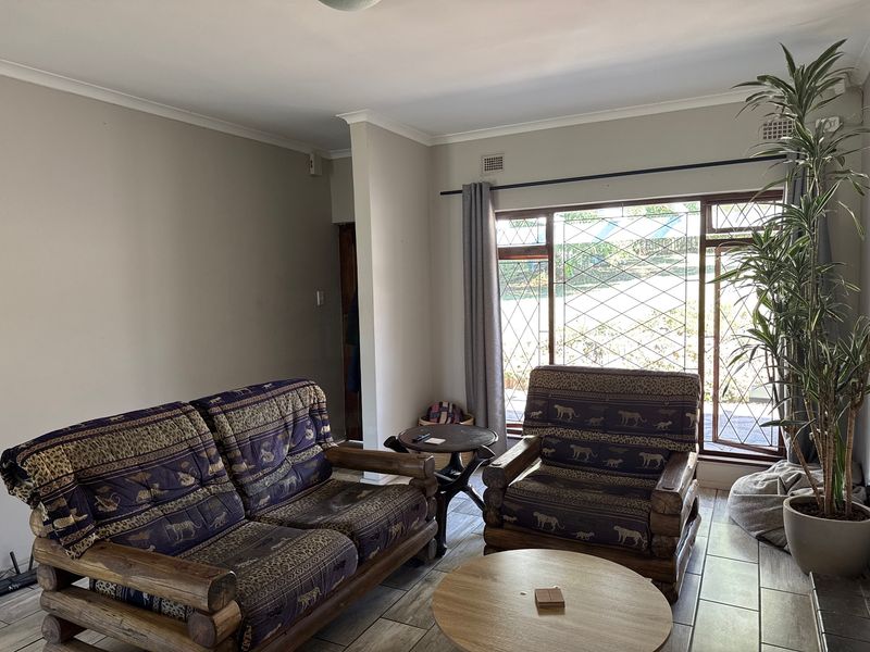 A comfortable living room featuring tiled flooring, large windows with security bars, and neutral wall finishes, providing a bright and functional space.