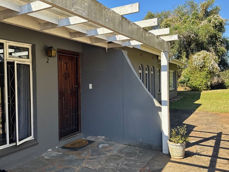 Front entrance of the cottage featuring a stone paved patio, a wooden front door with security gate, and a timber pergola structure.