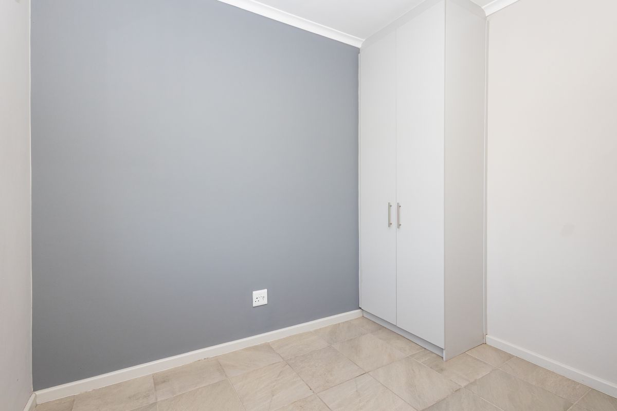 A clean, empty bedroom featuring neutral grey accent wall, built-in white wardrobe, and tiled flooring.