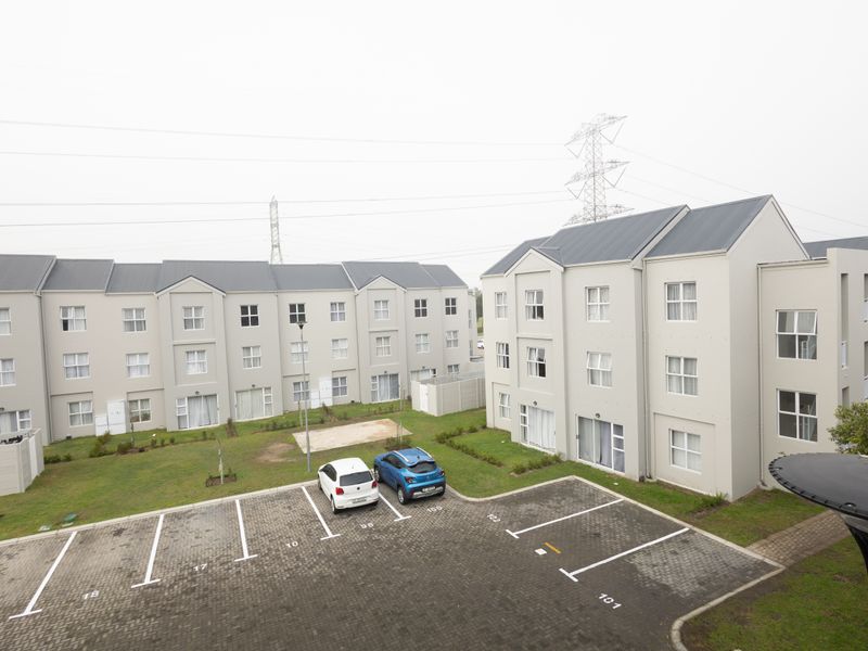 An elevated view of the apartment complex exterior, featuring a paved parking area, landscaped grounds, and multi-story residential buildings with metal roofing.