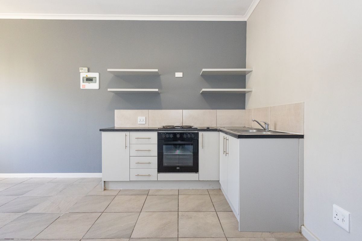 A compact, modern kitchen featuring built-in cabinetry, an integrated oven and hob, tiled splashbacks, and neutral grey wall finishes.