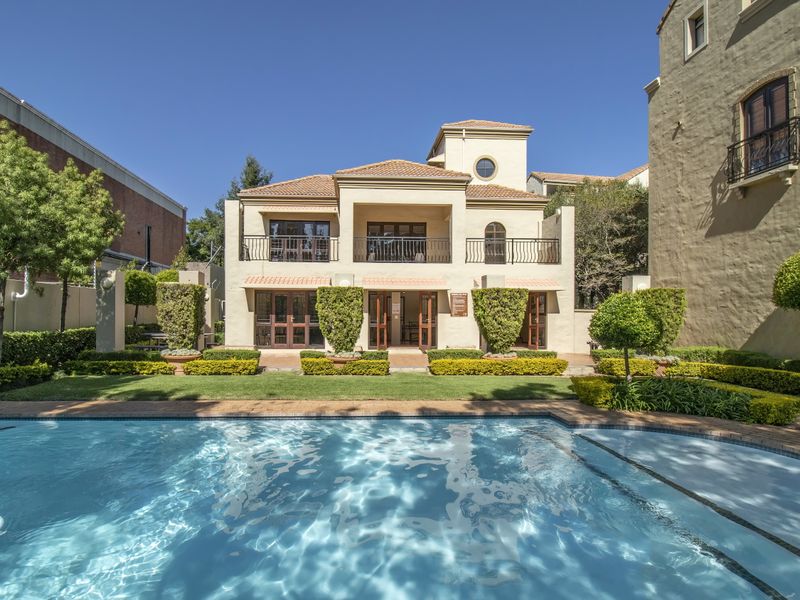 A well-maintained exterior view of an apartment complex featuring a swimming pool, landscaped garden, and a multi-story building with balconies.