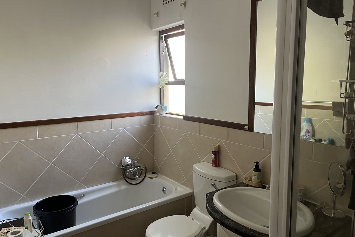 A functional bathroom featuring a bathtub, toilet, and vanity with a mirror, finished with neutral wall tiling and a top-hung window.