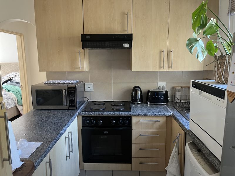 Compact kitchen featuring light wood-finish cabinetry, granite-look laminate countertops, a built-in oven with electric hob, and a tiled backsplash.