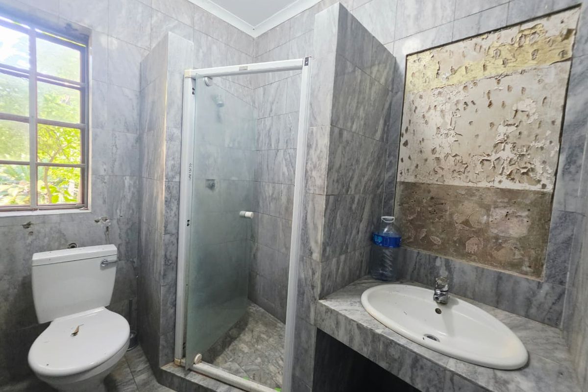 A bathroom featuring a shower enclosure, built-in vanity with basin, and toilet, currently requiring repairs to the wall surface above the vanity.