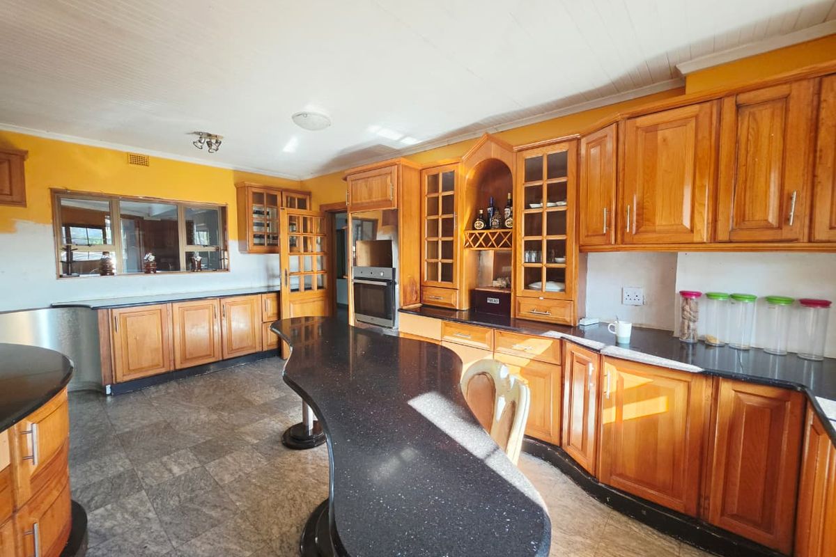 Spacious kitchen featuring extensive wooden cabinetry, black granite countertops, a large central island, and a convenient pass-through window to the adjacent living area.