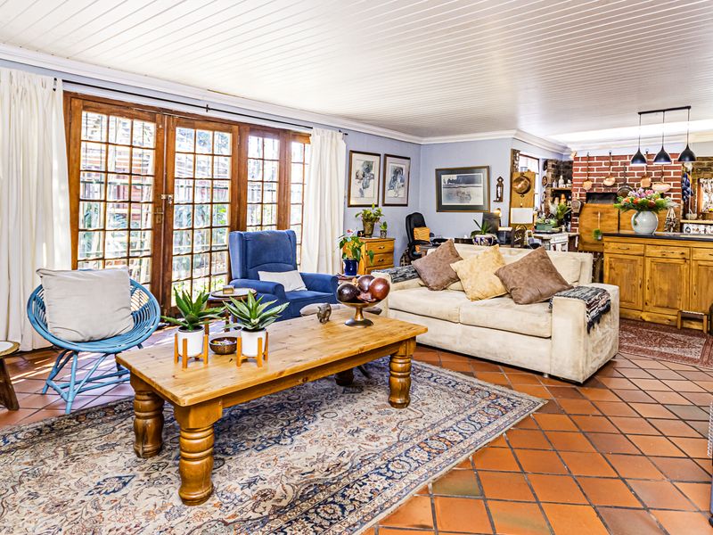 Spacious open-plan living area featuring terracotta floor tiles, a timber panelled ceiling, and direct access to the garden through timber-framed french doors.
