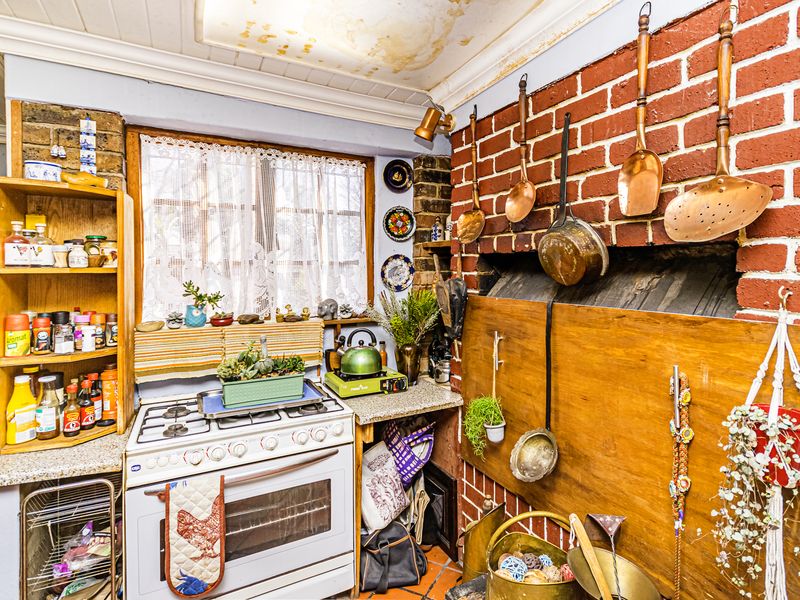 A rustic kitchen featuring an exposed brick wall, gas stove, and oven, with visible water damage on the ceiling requiring maintenance.