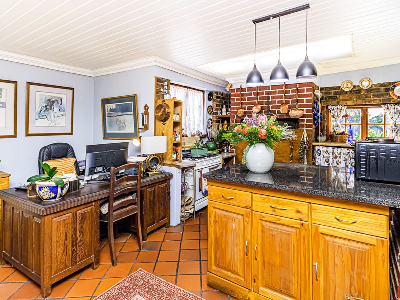 Open-plan kitchen and workspace featuring exposed brick walls, granite countertops, wooden cabinetry, and terracotta floor tiles under a tongue and groove ceiling.