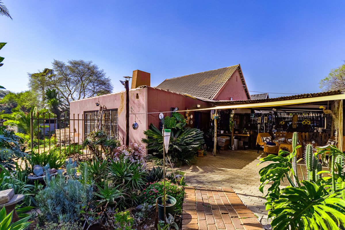 Rear view of the property featuring a brick-paved patio area, covered outdoor space, and established garden surroundings.